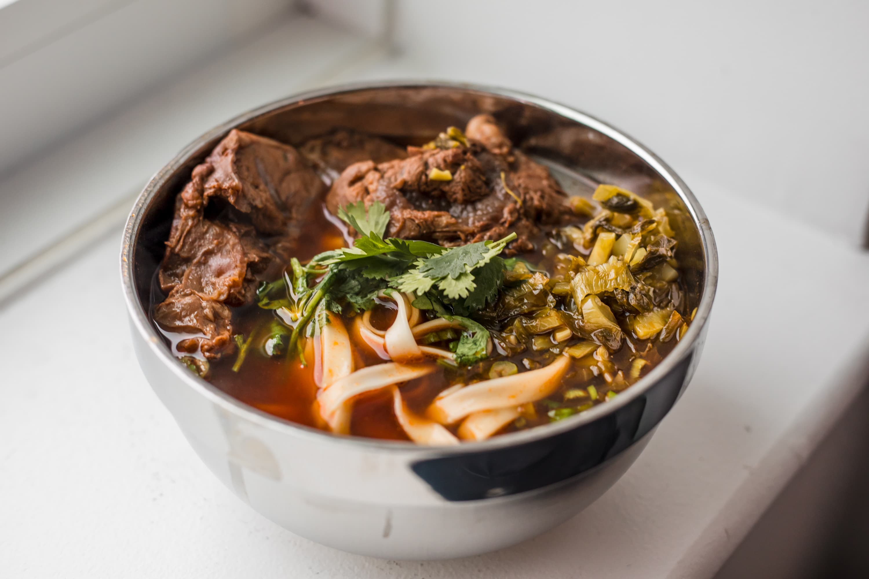 A bowl of Taiwanese beef noodle soup with noodles, beef shank, and cilantro