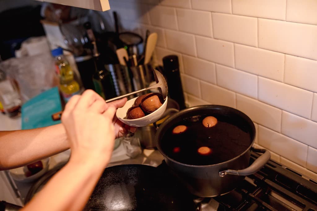 Tea eggs being scooped from a simmering pot into a white bowl